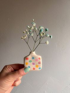 a hand holding a small ceramic vase with flowers in it's top and bottom