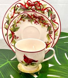 a white and red china set on top of a green leafy tablecloth with a cardinal design