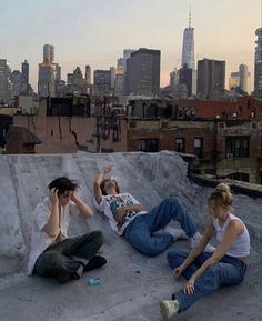 three people sitting on top of a roof talking on their cell phones in the city