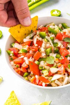 a hand dipping a tortilla chip into a bowl filled with salsa and veggies