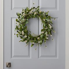 a wreath hanging on the front door of a house with white flowers and green leaves