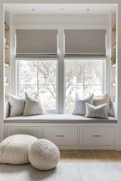 a window seat with two pillows on it in front of the windowsill and some shelves