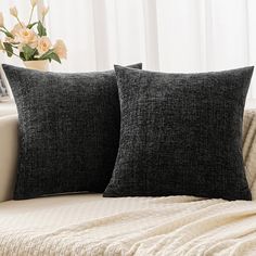 two black pillows sitting on top of a white couch next to a vase with flowers