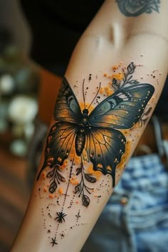 a woman's arm with an orange and black butterfly tattoo on her left arm