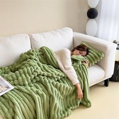 a woman laying on top of a white couch under a green blanket