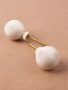 two white knobs are attached to gold - plated screws on a brown surface