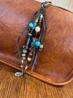 a brown leather bag sitting on top of a wooden table next to a purse with beads and charms hanging from it