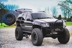 a black jeep parked on top of a gravel road next to a large monster truck