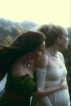 two women in white dresses standing next to each other with their arms around one another