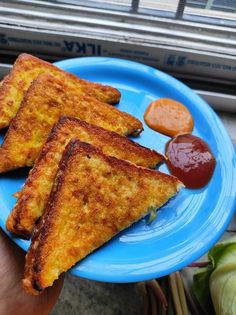 three pieces of grilled cheese on a blue plate with ketchup and mustard