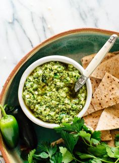 a bowl filled with guacamole surrounded by tortilla chips and green peppers