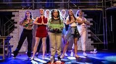 a group of women standing on top of a stage next to each other with their hands in their pockets