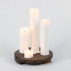 five white candles sitting on top of a piece of wood with one candle in the middle