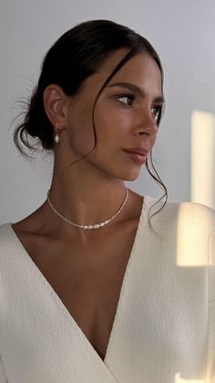 a woman wearing a white sweater with a necklace and earrings on her neck, looking off to the side