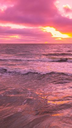 the sun is setting over the ocean with waves crashing in to shore and pink clouds