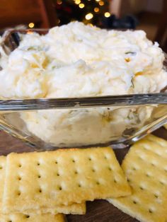 a glass bowl filled with white cheese and crackers on top of a wooden table