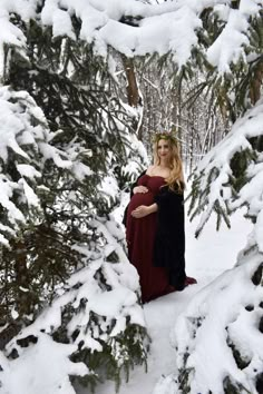 a pregnant woman is standing in the snow near some pine trees and looking at the camera