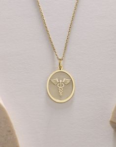 Gold Caduceus Pendant - Medical Gold Necklace ● Material of pendant: Solid Gold 14k ( REAL GOLD ) ● Metal Stamp: 14k ( REAL GOLD ) ● The pendant is available in 5 sizes: - 12x17 mm / 0,47 x 0,66 inches - 13x18 mm / 0,51 x 0,70 inches  In the photos - 14x19 mm / 0,55 x 0,74 inches  - 16x21 mm / 0,62 x 0,82 inches  - 18x24 mm / 0,70 x 0,94 inches ( In the photos the size is 13x18 mm / 0,51 x 0,70 inches ) ( Jump Ring inner diameter: 4 mm ) ● Material of chain: Solid gold 14k ( REAL GOLD ) It is thin and dainty and it is available in 4 sizes: - 40 cm / 15,75 inches ( Length ) - 45 cm / 17,72 inches ( Length ) In the photos - 50 cm / 19,68 inches ( Length ) - 55 cm / 21,65 inches ( Length ) ● Backside engraving is FREE ( Please use the personalization box for that.) ● If you want larger size, Symbolic Oval Charm Necklaces, Symbolic Oval Necklaces With Charms, Rod Of Asclepius, Doctor Jewelry, Caduceus Symbol, Nurse Jewelry, Dandelion Necklace, Gold Statue, Wanderlust Jewelry