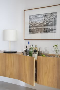 a wooden cabinet with bottles and glasses on it in front of a framed photograph above