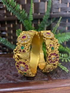 Temple bangle in matte gold and ruby stone. Detailing has the Rajasthani similarity. About an inch wide. Disclaimer: Price listed is for a single Kada. If you want to get them in a pair please select quantity 2. Gold Bracelet With Peacock Design As Gift, Gold Bracelets With Peacock Design As Gift, Festive Gold Bangle With Stone Setting, Festive Gold Bracelets With Stone Setting, Gold Peacock Design Bracelets For Festive Occasions, Gold Bracelet With Peacock Design For Festive Occasion, Gold Bracelet With Peacock Design For Festive Season, Gold Peacock Design Bracelet For Festive Occasions, Gold Bracelet With Stone Setting For Festivals