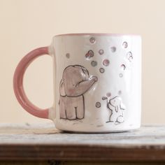 a pink and white coffee mug with an elephant on it's side sitting on a table