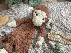 a crocheted monkey laying on top of a bed next to a wooden bead necklace