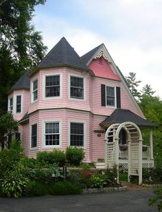 a pink house with black roof and white trim on the front porch, surrounded by trees