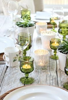 a wooden table topped with lots of white dishes and green cups filled with plants on top of it