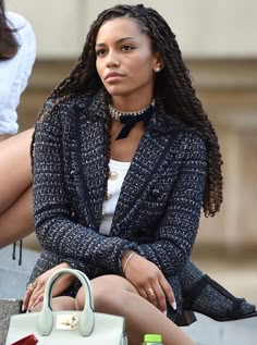 a woman sitting on the ground next to a handbag with her legs crossed in front of her