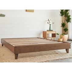 a wooden bed frame sitting on top of a rug in front of a white wall