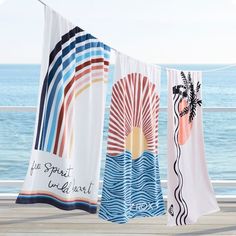 three beach towels hanging on a clothes line by the ocean with words written on them