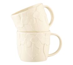 two white mugs sitting side by side on top of each other, one with leaves