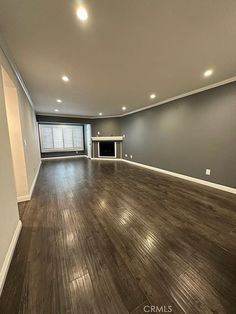 an empty living room with hard wood flooring and gray walls, along with a fireplace