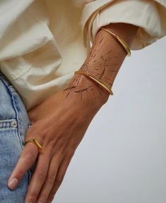 a woman's arm with a gold bracelet and dandelion tattoo on it