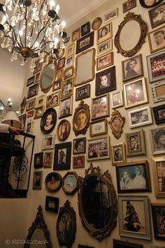 a wall full of pictures and framed photos with a chandelier hanging from the ceiling