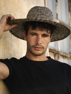 a man wearing a hat standing next to a wall with his hand on his head