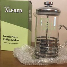 a french press coffee maker sitting on top of a wooden table next to a box