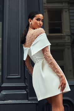 a woman in a white dress leaning against a black pole and posing for the camera