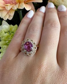 a close up of a person's hand with a ring on it and flowers in the background