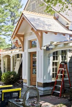 a man is working on the roof of a small white house with wood trimming