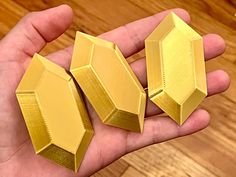 three gold colored objects in the palm of someone's hand on a wooden table