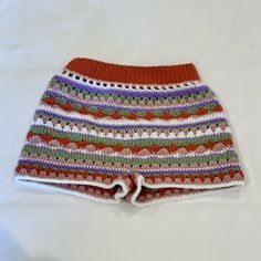 a crocheted shorts is laying on a white surface with an orange, pink, green and purple striped pattern