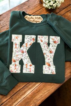 a green sweater with the letter ky on it sitting on top of a wooden table