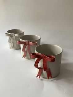 three white cups with red bows on them