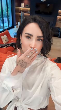 a woman with tattoos on her left hand is posing in front of a couch and looking at the camera