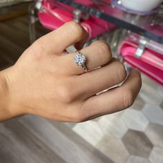 a woman's hand with a diamond ring on top of her finger, in front of a pink chair