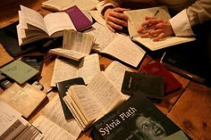 many books are spread out on the floor with one person holding a pen and writing