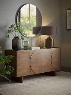 a round mirror is on the wall above a wooden cabinet with a plant in it