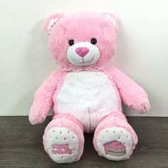 a pink and white teddy bear sitting on top of a wooden table next to a wall