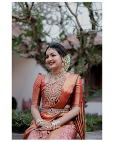 a woman in an orange and gold sari sitting on the ground with her hands clasped to her chest